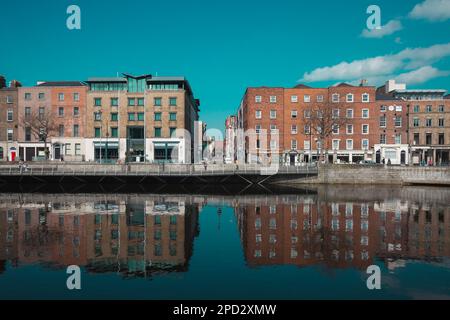 Dublino / Irlanda : gli edifici si riflettono in una calma acque del fiume Liffey lungo Ormond Quay a Dublino durante una giornata di primavera irlandese molto soleggiata Foto Stock