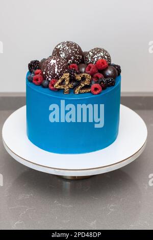 Bella torta di compleanno blu decorata con corona di mirtilli e lamponi, palline di cioccolato e numeri Foto Stock