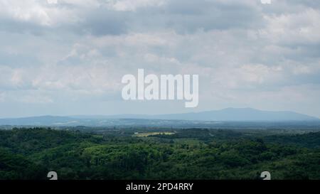 Campagna paesaggio collinare con villaggi durante il giorno nuvoloso, punto di sole sulla foresta e silhouette di montagna in foschia Foto Stock