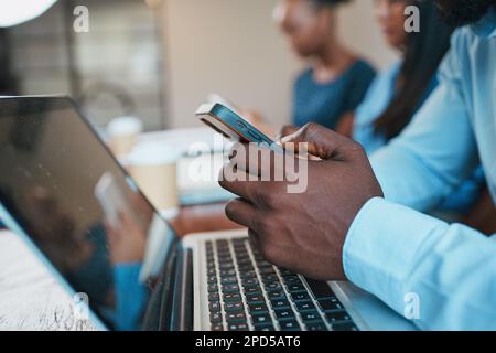 Primo piano delle mani dell'uomo nero che usa il telefono durante una riunione, con il computer portatile Foto Stock