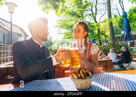 Una coppia felice che si siede nel Beer Garden o nell'oktoberfest e che si gode un bicchiere di birra e il sole Foto Stock