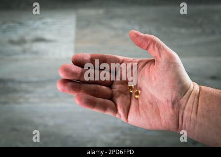 Mano dell'uomo che tiene due pillole di vitamina giallo dorato nel palmo Foto Stock