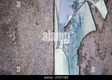 Uno specchio rotto su una parete industriale in cemento Foto Stock