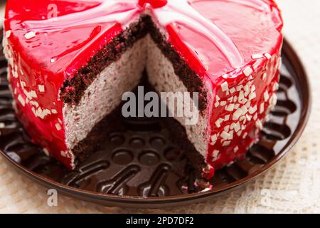 Tagliare la torta di ciliegia, una deliziosa e dolce confezione con glassa bianca rossa, briciole di cioccolato bianco e ciliegie si trova sul tavolo coperto da una tovaglia Foto Stock