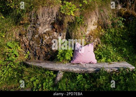 panca in legno realizzata a mano con cuscino contro la roccia sovrapposta al sole del tardo pomeriggio Foto Stock