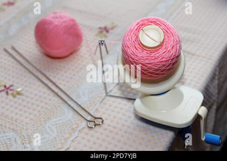 Processo di avvolgimento del filato di lana rosa dal groviglio all'avvolgimento, utilizzando un avvolgitore sul tavolo Foto Stock
