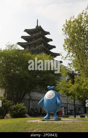 Blue Kawaii (carino) personaggio coreano / figura nei giardini del Museo Nazionale del Folclore di Corea a Seoul; torre del museo sullo sfondo Foto Stock