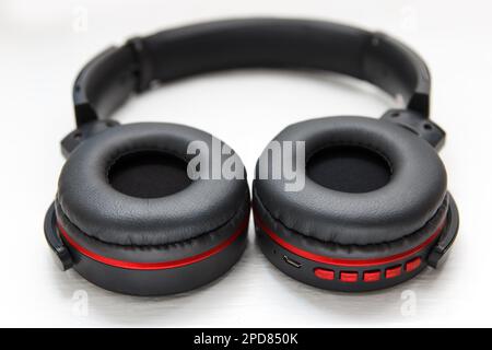 Le moderne cuffie stereo nere wireless si trovano su uno sfondo bianco, primo piano. Tecnologia audio alla moda molto comoda Foto Stock
