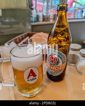 03 14 2023 - Atene, Grecia. Bicchiere e bottiglia di una fredda birra greca Alfa con una schiuma in un pub locale ad Atene, in Grecia Foto Stock