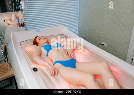 Felice giovane donna che indossa bikini sdraiato con gli occhi chiusi sul letto massaggio elettrico, avendo riposo godendo la procedura spa al salone di lusso spa. Foto Stock