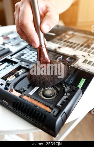 Repaiman con spazzola sta pulendo parti di laptop smontate. Supporto tecnico e risoluzione dei problemi relativi ai gadget. Manutenzione, riparazione, pulizia, manutenzione dei calcolatori. Officina di riparazione. Manutenzione hardware Foto Stock