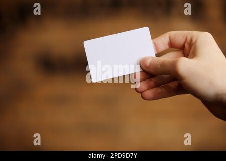 La mano maschio tiene il mockup bianco della scheda sullo sfondo della parete del mattone. Braccio di supporto modello per scheda telefonica semplice. Parte anteriore del display della scheda di credito in plastica. Controllare il design della scheda offset. Branding aziendale Foto Stock