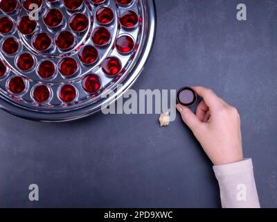 Primo piano della giovane donna che prende comunione il simbolo del vino del sangue di Gesù Cristo in coppette su fondo nero. Pasqua e cena del Signore conce Foto Stock