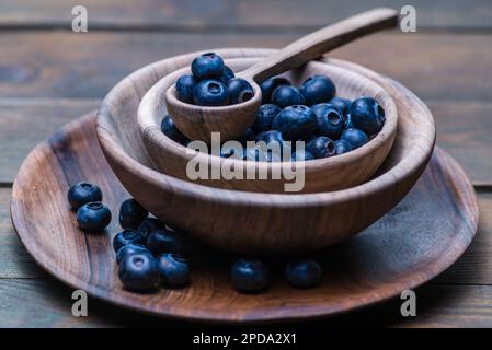 cucchiaio di legno maturo dolce mirtillo ciotola su tavola di legno rustico scuro. Sfondo fresco di mirtilli con spazio di copia per il testo. Vegan e vegetariano con Foto Stock