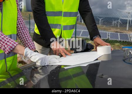 Primo piano delle mani di due ingegneri che analizzano un disegno tecnico in una centrale a energia solare. Foto Stock