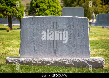 Lapide di granito decorato con una grande croce cristiana in un cimitero Foto Stock