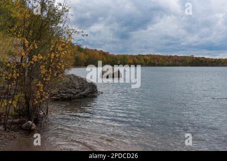 Panorama sul lago con foresta autunnale e grandi pietre in primo piano Foto Stock