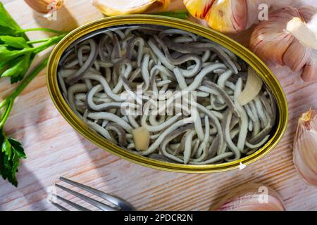 Aprire lattina di anguille sottaceto e aglio con verdure a tavola Foto Stock