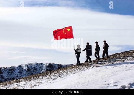 ALTAY, CINA - 14 MARZO 2023 - gli ufficiali di polizia detengono bandiere nazionali mentre pattugliano il confine su una montagna innevata in Altay, provincia dello Xinjiang, Cina Foto Stock