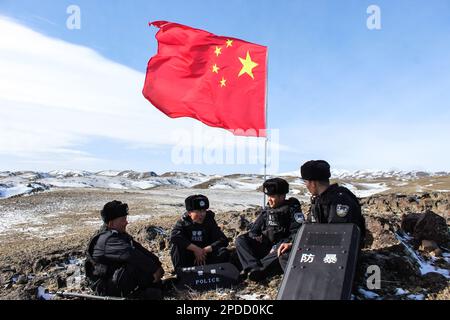 ALTAY, CINA - 14 MARZO 2023 - gli ufficiali di polizia detengono bandiere nazionali mentre pattugliano il confine su una montagna innevata in Altay, provincia dello Xinjiang, Cina Foto Stock