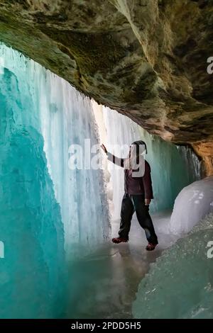 Karen Rentz esplorando dietro le tende formazione di ghiaccio utilizzato dagli arrampicatori di ghiaccio in Pictured Rocks National Lakeshore vicino a Munising, Upper Peninsula, Mah Foto Stock