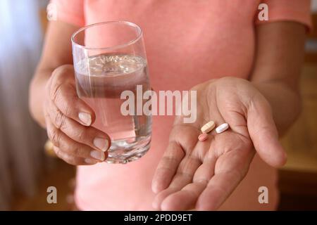 prendere pillole, donna tenendo pillole e bicchiere d'acqua nelle sue mani Foto Stock