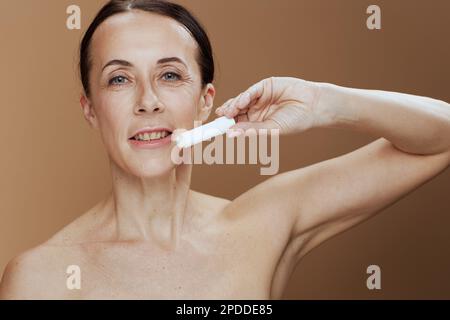 donna moderna con rossetto igienico su sfondo beige. Foto Stock