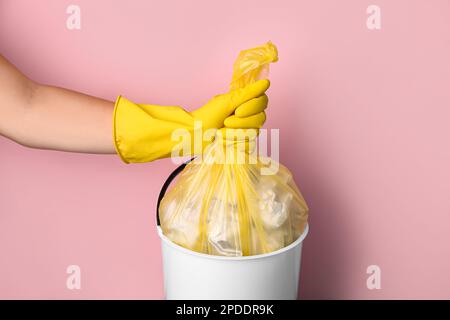 Donna che prende il sacchetto di immondizia dal bidone di immondizia su sfondo rosa Foto Stock