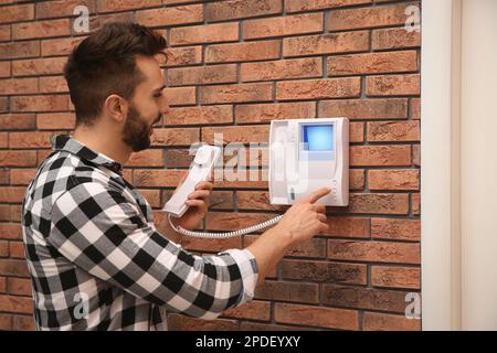 Uomo che preme il pulsante sul pannello dell'interfono all'interno Foto Stock