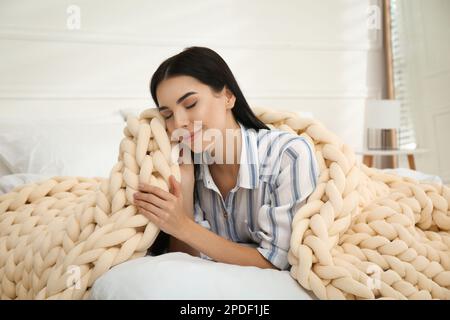 Giovane donna con coperta a maglia a letto a casa Foto Stock