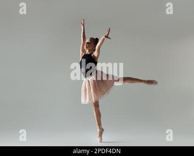 Simpatico piccolo ginnastica in gonna che si esibisce su sfondo bianco Foto Stock