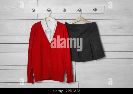 Camicia, jumper e gonna appesi su una parete di legno bianco. Uniforme scolastica Foto Stock