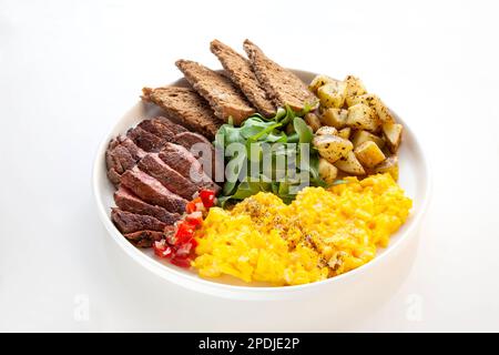 Filetto di manzo con uova strapazzate, foglie di rucola e patate con un lato di pane di segale. Foto Stock