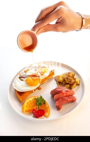 Colazione con uova fritte su waffle con salsicce di sciroppo d'acero e patate. Foto Stock