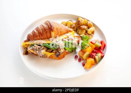 Panino di croissant con uova strapazzate con frutta e patate. Foto Stock