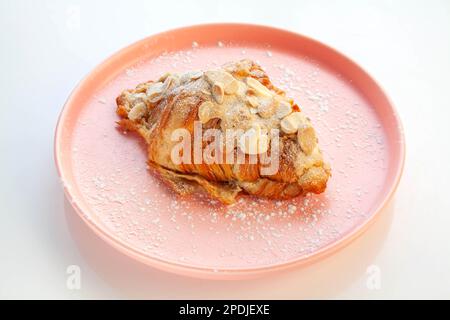 Croissant alle mandorle posto su un piatto rosa. Foto Stock