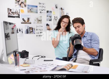 Alla ricerca dell'immagine migliore. Un fotografo che guarda le sue immagini nel suo ufficio con il suo assistente. Foto Stock