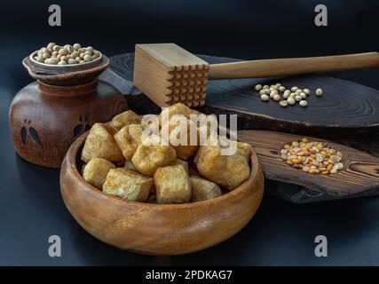Soffi di tofu fritti o tofu fritti in ciotola di legno e grani (soia) con fondo scuro. Spazio per il testo. Foto Stock