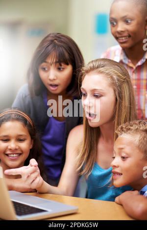 Insegnare loro la tecnologia. Un gruppo di alunni che lavorano su un computer portatile in classe con il loro tutor. Foto Stock