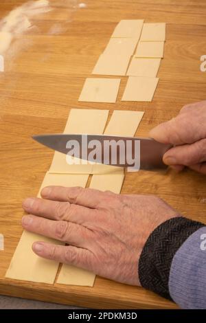 Produzione di pasta fatta in casa - tagliatelle italiane nel fai da te - primo piano delle mani che tagliano l'impasto per preparare la pasta fatta in casa Foto Stock