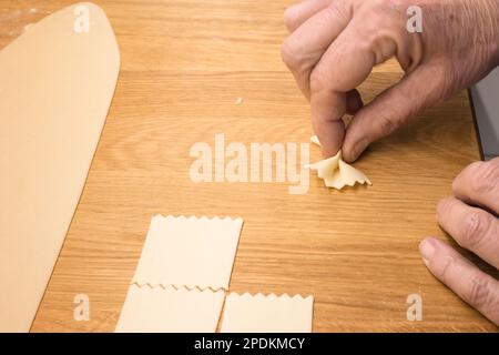 Produzione di pasta fatta in casa - tagliatelle italiane (Farfalle) in diy - primo piano di una mano che spreme l'impasto per preparare la pasta farfalle fatta in casa Foto Stock