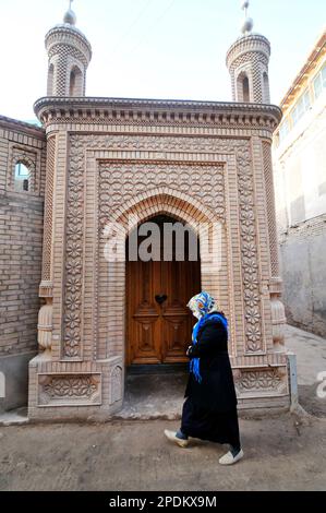 Una donna uighur che cammina vicino a una piccola moschea nella città vecchia di Kashgar, Xinjiang, Cina. Foto Stock