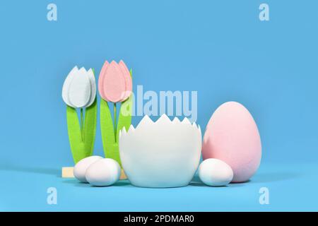 Sfondo digitale neonato con guscio d'uovo bianco con uova di Pasqua e fiori di tulipano feltro sullo sfondo Foto Stock