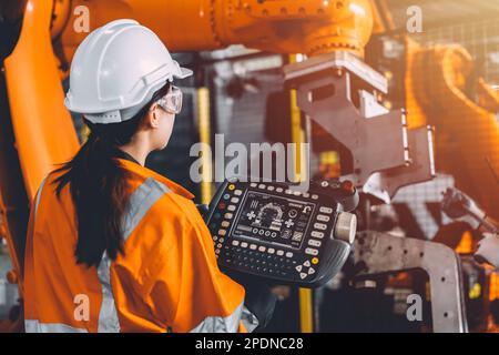 Team di tecnici addetti alla manutenzione della saldatura robotizzata che lavora nello stabilimento di automazione. Una donna operatrice utilizza il controller manuale del software del braccio robotico nella produzione automatizzata Foto Stock