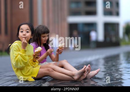 Due ragazze sedute, con gambe in fontana, gelato e giorno d'estate. Foto Stock