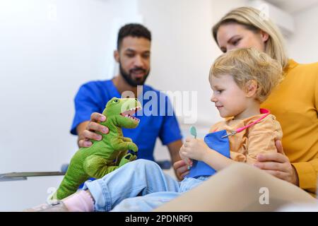 Giovane dentista multirazziale che gioca con i bambini nel suo ufficio. Foto Stock