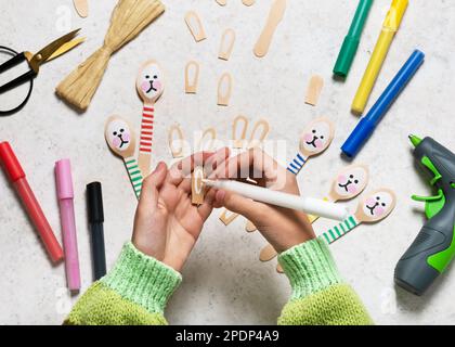 Passaggio 7. Dipingere le orecchie su una forcella con un pittore acrilico bianco. Rendere grazioso coniglietto decorazione da cucchiaio di legno per Pasqua con i bambini. Vista dall'alto. Foto Stock