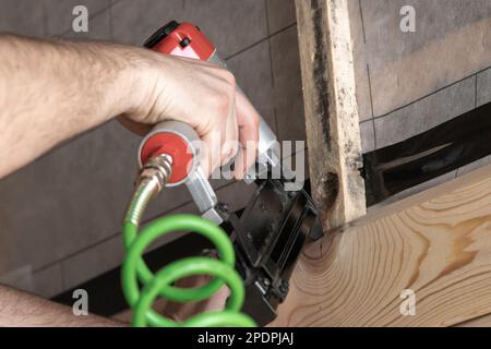 Mani di uomo tagliate che lavorano con la graffatrice, pistola per chiodi con cavo verde e asse di legno. Graffatura e graffatura di graffette metalliche, facendo la disposizione su asse di legno Foto Stock