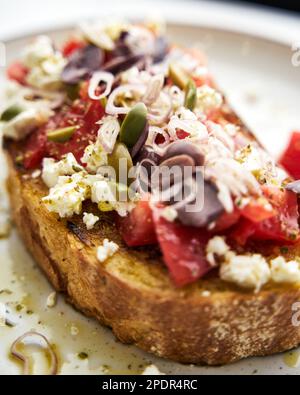 Dakos insalata tradizionale greca insalata con fette biscottate di orzo o pane ammollato e croccante, condita con pomodori succosi, formaggio feta, cipolle, olive, e un Foto Stock