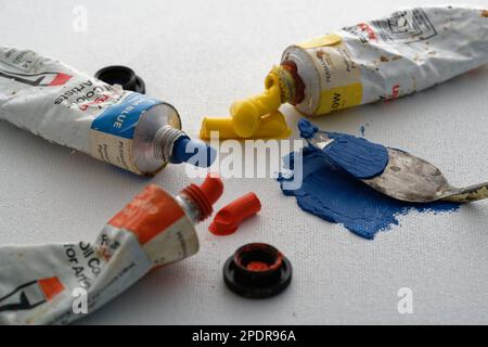 Vernici a olio colorate e un coltello a palette su uno sfondo di tela. Blu, rosso e giallo per creare una foto. Il processo creativo. Foto Stock